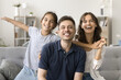© fizkes - Cheerful happy parents and kid with open flying arms having fun on home couch, looking at camera with toothy smiles, enjoying family leisure, together, laughing. Video call screen, head shot portrait