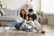 © fizkes - Cheerful excited parents tickling beloved kid girl, playing with child on heating floor in modern home interior, sitting on carpet, laughing, shouting for joy, enjoying family leisure
