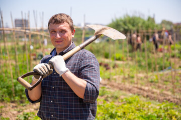 Wall Mural - Man professional horticulturist with garden shovel working at land in garden