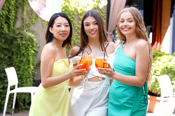 Wall Mural - Beautiful young women with glasses of tasty aperol spritz cocktail spending time in cafe, outdoors