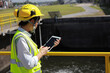 © naraichal - a female engineer is wearing a protective helmet on her head, using tablet Analytics engineering data. at the wastewater treatment plant