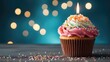 small colorful birthday cupcake with candle on pastel blue background.
