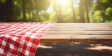 Picnic Table With A Red Checkered Towel, Empty Space, And A Blurred Wooden Deck Backdrop. Promotion Display.