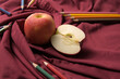 Apple on red cloth surrounded by colour pencils.