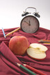 Apple on red cloth surrounded by colour pencils and a retro clock.