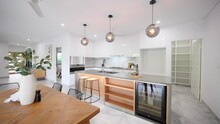 Large Open Kitchen With Wine Fridge. Pendant Lighting Chandeliers Over The Stone Bench. White And Grey Kitchen With Gas Stove