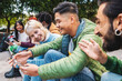 © Lomb - A group of diverse friends laugh and share content on a smartphone while sitting together in an urban outdoor setting, portraying modern connectivity and friendship.