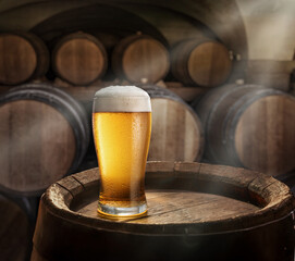 Sticker - Glass of beer on top of  wooden barrel and  wood barrels in cellar at the background. Sun ray falling down to it surface. Placement for your product.