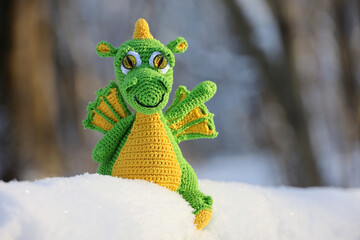 Wall Mural - Knitted dragon in a snow on winter forest background, greeting card. Symbol of Chinese New Year 2024