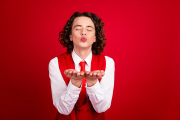 Poster - Photo of yong gentleman funny curly guy in vest with necktie dreaming and send air kisses hold arms isolated over red color background