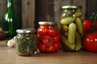 Salted red tomatoes and green gherkins in jars on a light wooden background