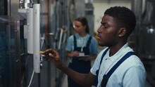 Tilt Side Footage Of African American Engineer In Polo Shirt And Jumpsuit Adjusting Mechanism Operation Using Sensor Monitor In Service Room At Plant