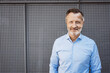 © contrastwerkstatt - Successful Bestager Businessman in Blue Shirt Smiles Confidently Against Metal Wall Background.