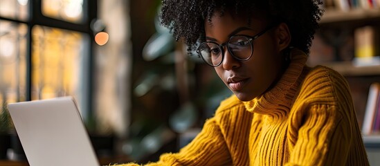 Thoughtful Black software developer in her 30s deeply engaged in coding on her laptop in a spacious coworking area a modern tech professional in autumn. Copy space image. Place for adding text