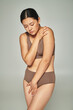 © LIGHTFIELD STUDIOS - sad asian woman in underwear covering body while embracing herself on grey backdrop, body shaming