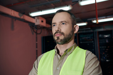 Wall Mural - attractive pensive specialist in safety vest posing and looking away while working in data center