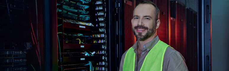 Wall Mural - good looking jolly man in safety vest smiling at camera during inspection, data center, banner