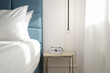 Blue king size bed with crisp white bedding and digital alarm clock on the nightstand under beautiful morning sunlights	