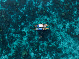 Fototapeta Sypialnia - View from above, stunning aerial view of two long tail boats floating on a turquoise water while some tourists snorkel.  Phuket, Thailand.