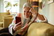 © Marko Geber - Smiling elderly woman using smartphone on home sofa