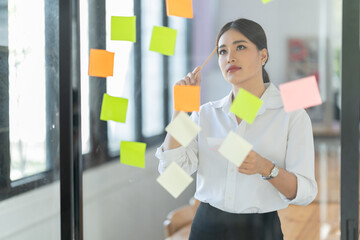 Wall Mural - Portrait of beautiful young woman standing in front of glass board and smiling on camera. Female office worker using laptop in company.