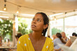 © Julian - A beautiful young Hispanic woman, dressed in a yellow dress with white dots, sitting in a restaurant, looking indirectly thinking she is going to order