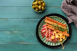© kasia2003 - Slices of prosciutto or jamon. Antipasto Delicious grissini sticks with prosciutto, cheese, rosemary, olives on green plate on old wooden blue background. Appetizers table with italian snacks Top view