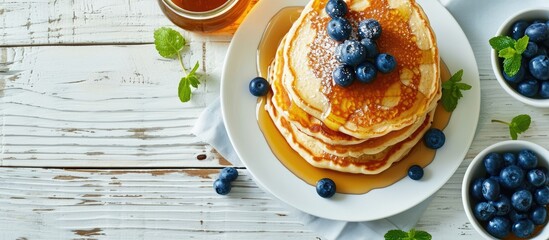 Kid s breakfast meal pancakes blueberries and maple syrup Plate in child s hands on white wooden table Captured from above top view flat lay. Copy space image. Place for adding text