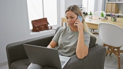 Poster - Young woman working remotely in a modern office while talking on the phone and using a laptop