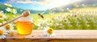 Honigglas mit Holzlöffel und Biene vor Blumenwiese 