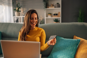 Woman buying online on a laptop while sitting on a sofa at home