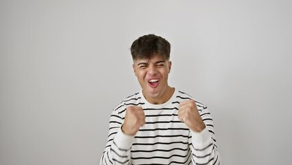 Wall Mural - Cheerful, confident young hispanic man in stripes celebrates big win with a joyful scream and winner's gesture against an isolated white background