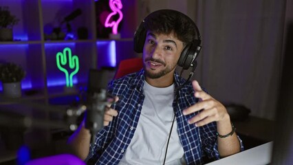 Wall Mural - Young arab man, smiling streamer speaking during night time video call, dominating the gaming universe from his dark gaming room, engaged in breathtaking virtual entertainment