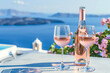 Bottle of pink wine with glass, with Santorini seascape background in pastel colours, romantic story. With space for text. Advertising photo.