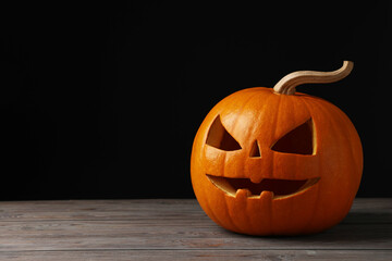 Wall Mural - Scary jack o'lantern made of pumpkin on wooden table against black background, space for text. Halloween traditional decor