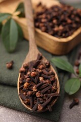 Wall Mural - wooden spoon with aromatic cloves and green leaves on table, closeup