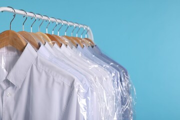 Wall Mural - Dry-cleaning service. Many different clothes in plastic bags hanging on rack against light blue background, closeup and space for text