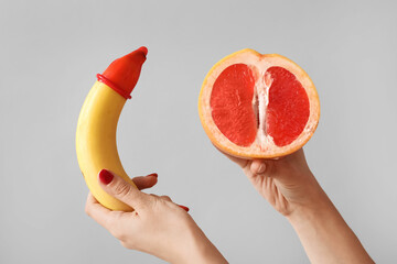 Canvas Print - Woman with banana in condom and half of grapefruit on light background. Sex concept