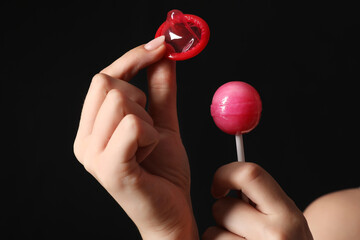 Wall Mural - Young woman with lollipop and condom on dark background, closeup. Sex concept