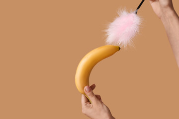 Wall Mural - Young woman with banana and feather stick on beige background. Sex concept