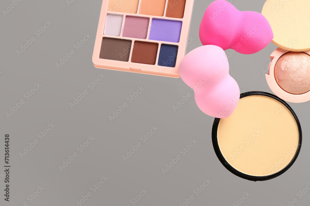 Flying makeup sponges and cosmetics on grey background