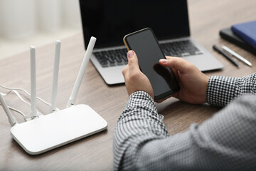 Man with smartphone and laptop connecting to internet via Wi-Fi router at wooden table, closeup