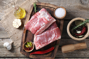 Pieces of raw pork belly, oil, garlic, salt and spices on wooden table, flat lay