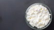 Cottage cheese in a glass bowl on a grey background, top view