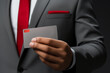 Cropped portrait of a businessman in a dark formal suit and tie, holding a bank card in his hand in front of him. Successful entrepreneur uses a credit card. Cashless payment concept. Mockup.