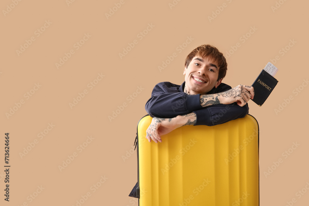 Happy young man with passport, ticket and suitcase on color background