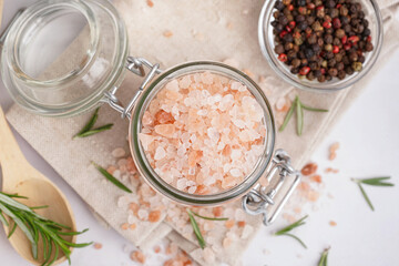 Jar with Himalayan pink salt and glass bowl of peppercorn on white background