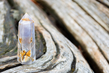 Wall Mural - A close up image of a blue lace healing crystal tower standing on a faded and cracked driftwood log. 