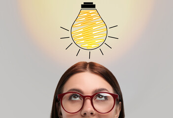 Wall Mural - idea generation. woman looking at illustration of glowing light bulb over her on light background