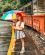 Little girl smiling holding a rainbow umbrella in her arms with vintage train on the background. Puffing Billy station, train adventure in Melbourne, Australia. Beautiful toddler girl portrait. 